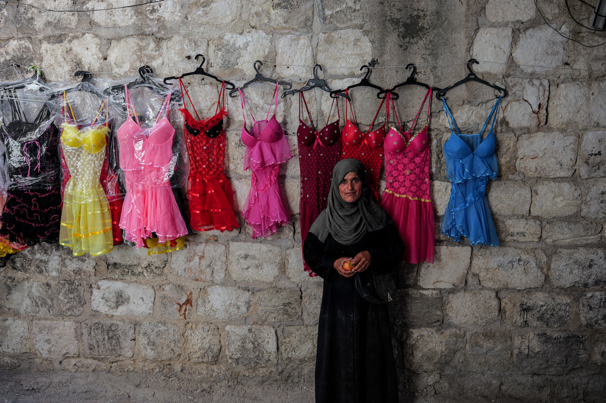 Eine Frau unter einer Reihe bunter Kleider in Syrien