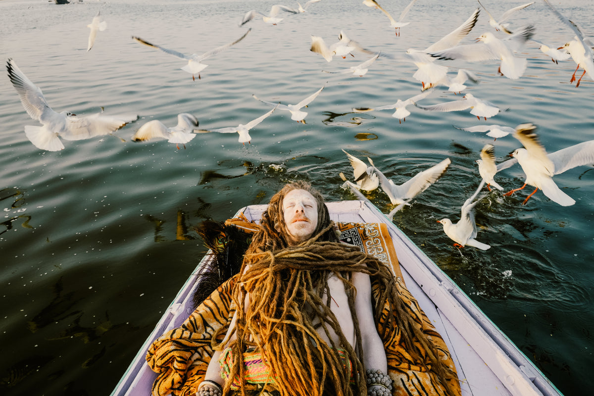 Ein Mann liegt in einem Boot, während Vögel über dem Wasser fliegen, Indien