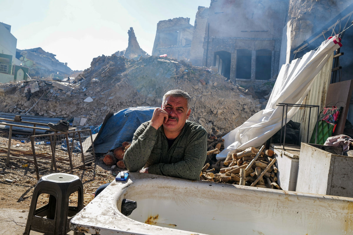 Ein Mann neben einer Badewanne zwischen beschädigten Gebäuden im Irak