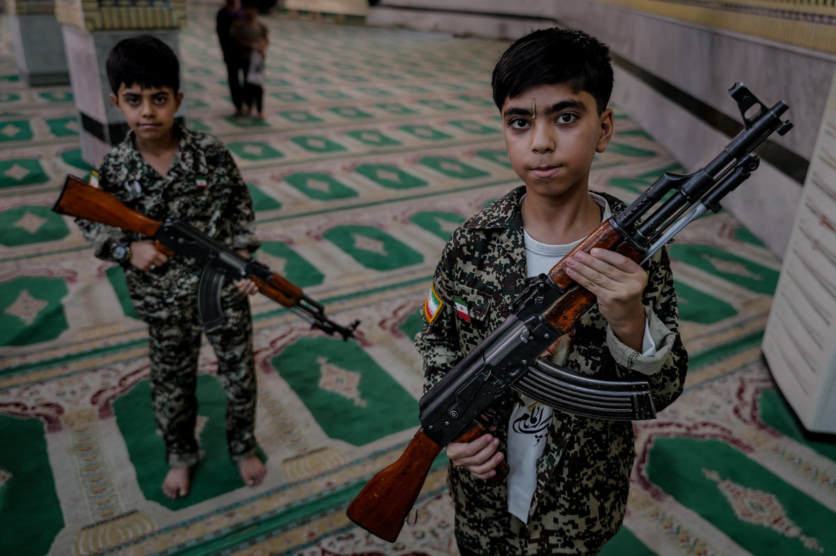 Two boys in camouflage hold rifles inside a prayer hall