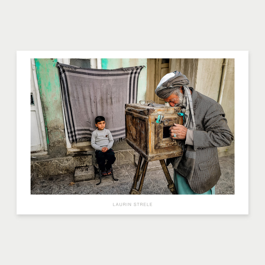A1 poster of Kabul Photographer, Afghanistan, by Laurin Strele, showing a wooden box camera and seated boy within a white border.