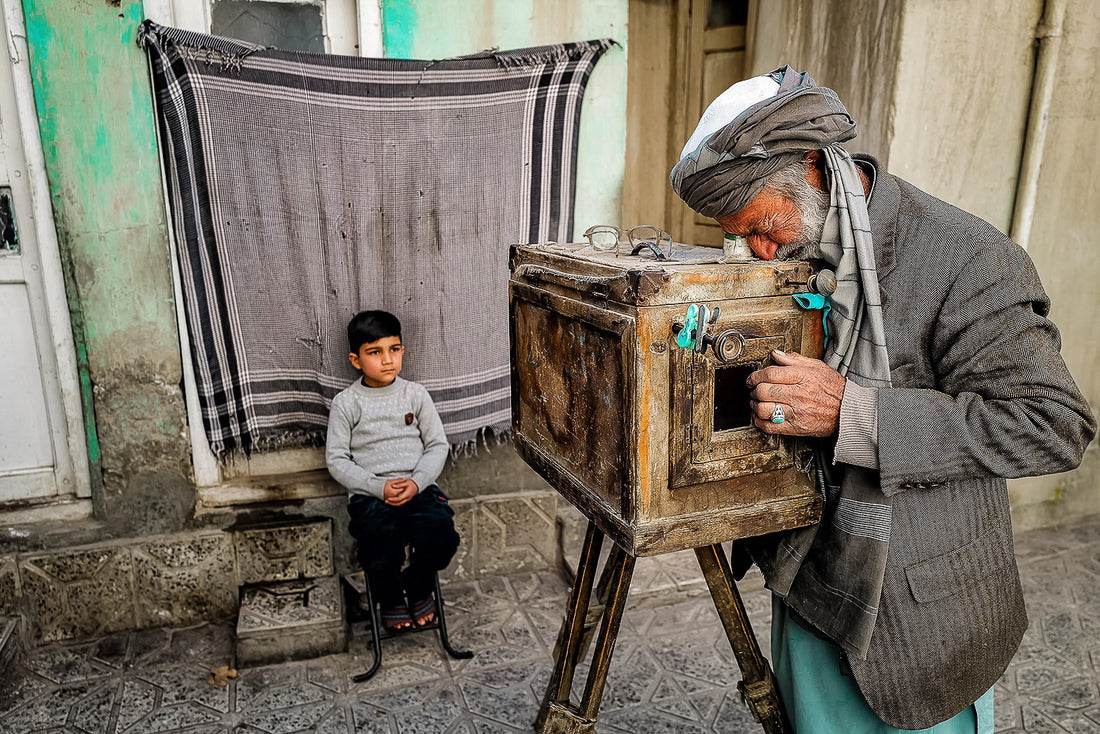 A1 poster of Kabul Photographer, Afghanistan, by Laurin Strele, showing a wooden box camera and seated boy within a white border.
