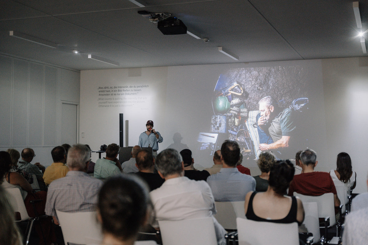 Laurin Strele speaking to an audience beside a projected documentary photograph.