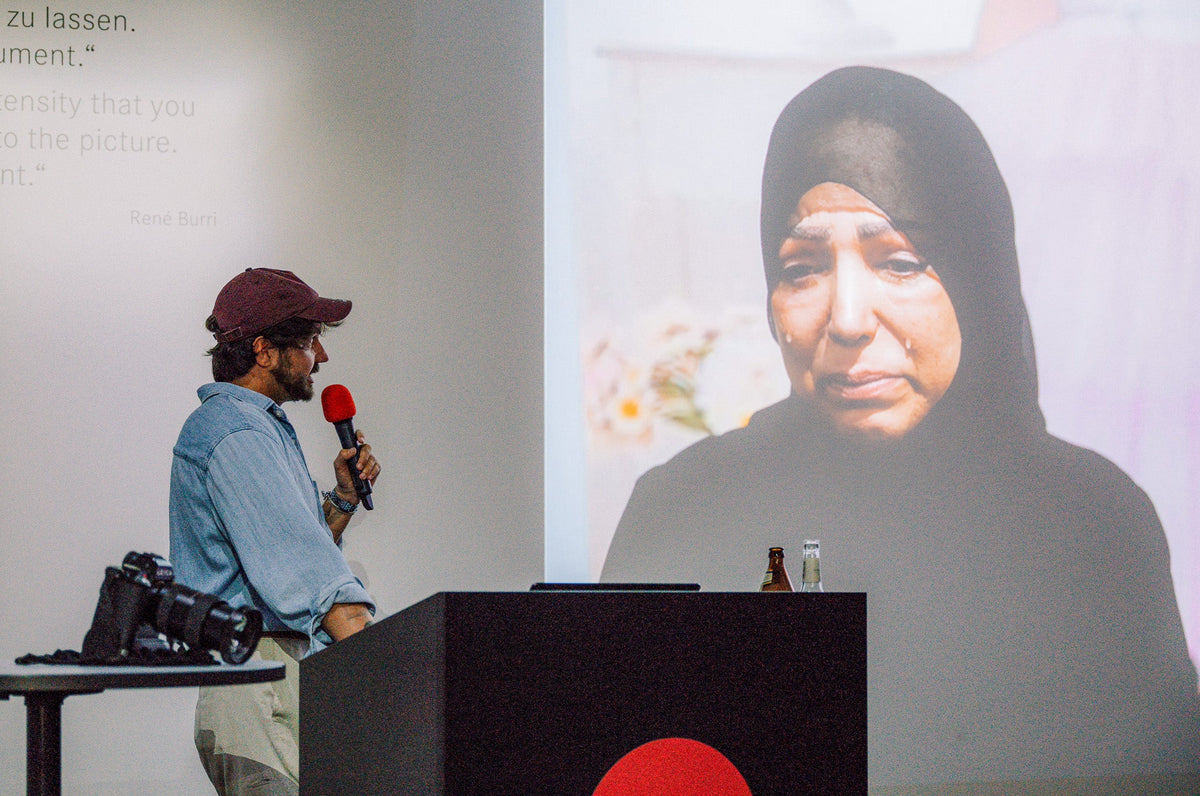 Laurin Strele speaking into a microphone beside a projected documentary portrait.