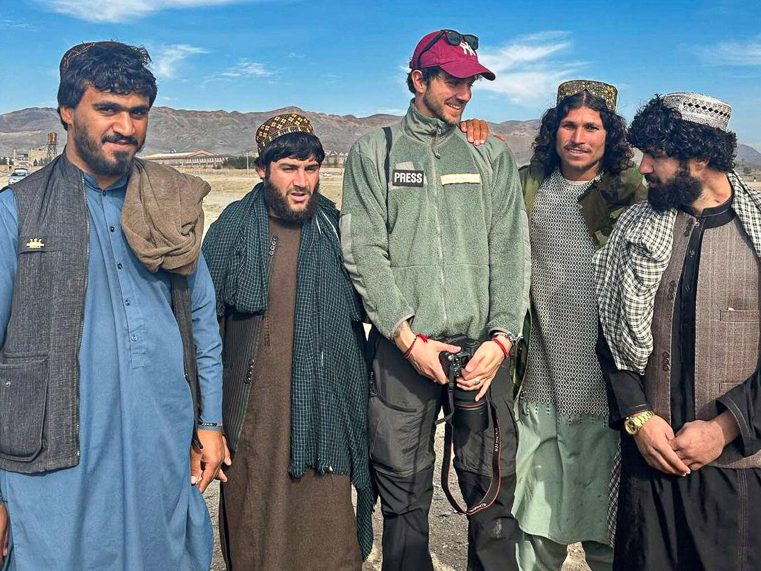A photographer poses with four men in front of a mountain landscape.