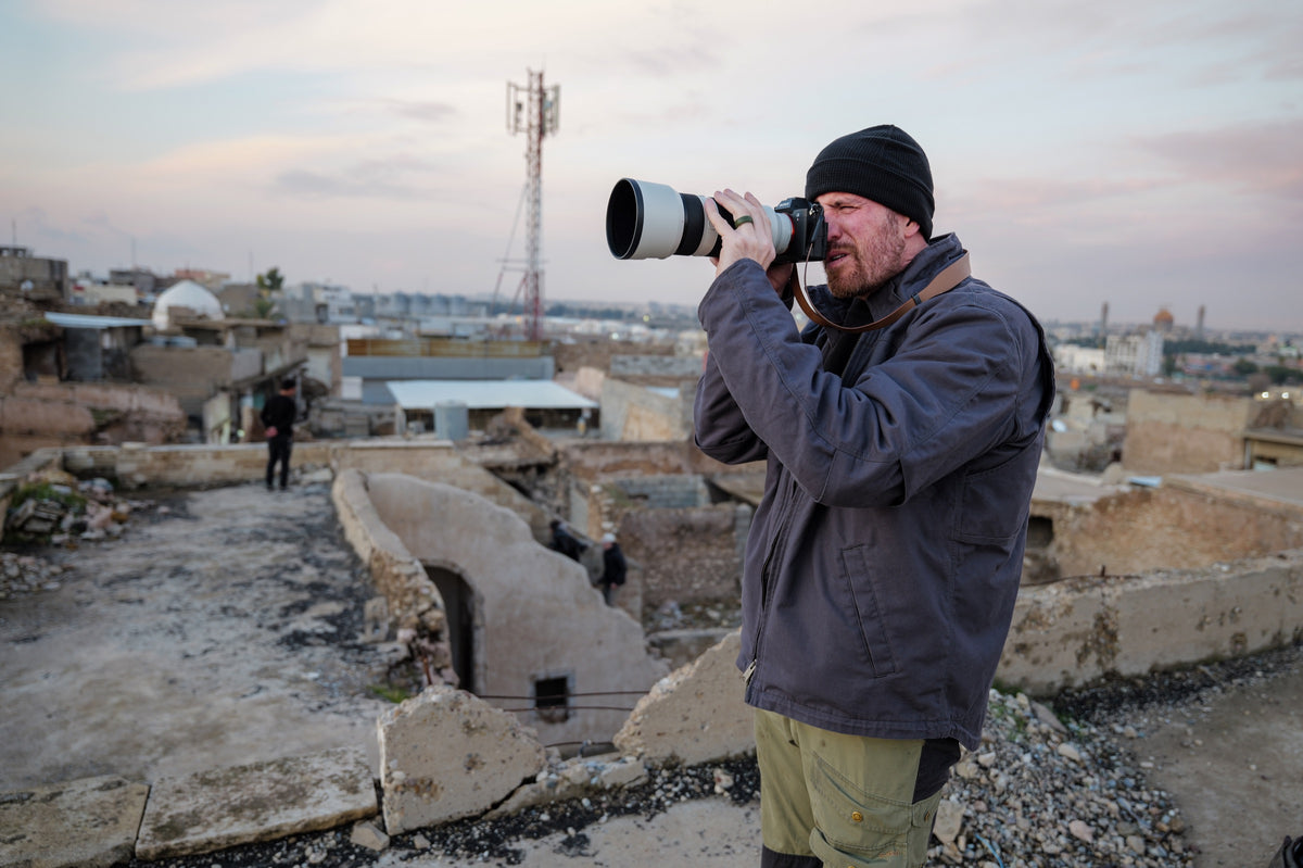 A photographer with a telephoto lens photographs a city from a rooftop.