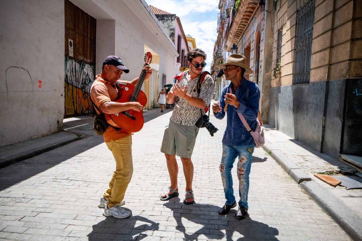 A photographer joins two street musicians on a sunlit street.