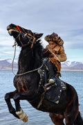 A young rider guides a rearing horse beside a mountain lake in western Mongolia, 2023. Photograph by Laurin Strele.